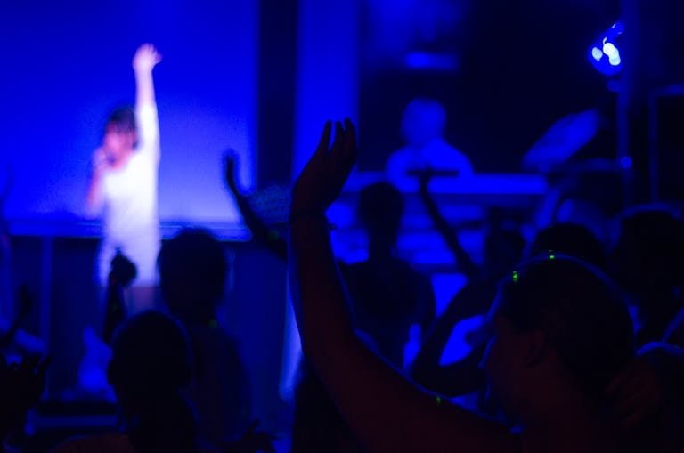 A dynamic nightclub scene with a live performance, vibrant crowd, and blue ambient lighting.